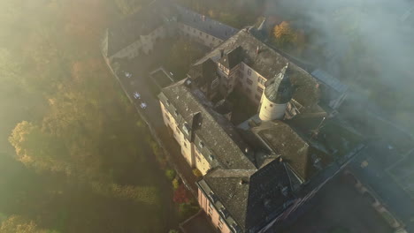 Aerial-top-down-shot-of-historic-german-castle-in-dense-fog-during-sunset