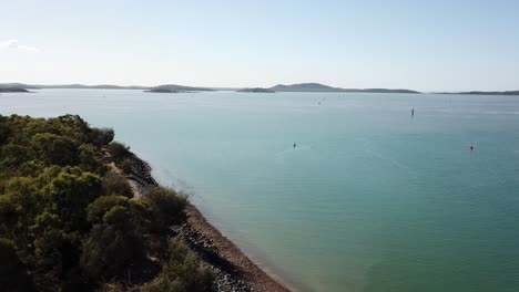 Drone-aerial-over-blue-ocean-with-mountains-in-the-background-on-sunny-day