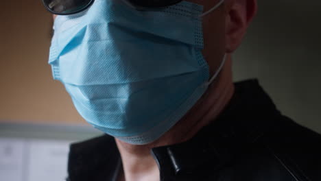 Man-wearing-a-covid-19-surgical-mask-standing-inside,-looking-outside
