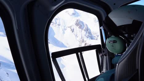 Helicopter-Pilot-Looking-Out-The-Side-Window-At-Bright-White-Snowy-Rocky-Mountains