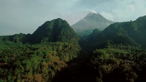 Lush-hills-overgrown-with-plants-in-deep-jungle-of-Indonesia-and-smoking-Volcano-in-background