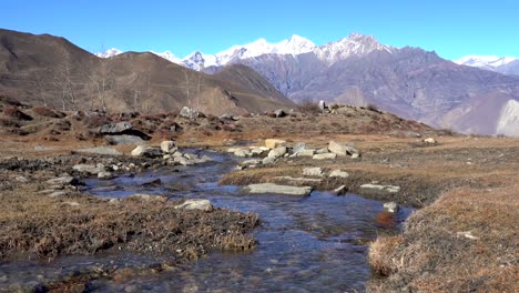Ein-Kleiner-Bach,-Der-Einen-Hügel-Mit-Den-Bergen-Des-Himalaya-Im-Hintergrund-In-Der-Region-Mustang-In-Nepal-Hinunterfließt