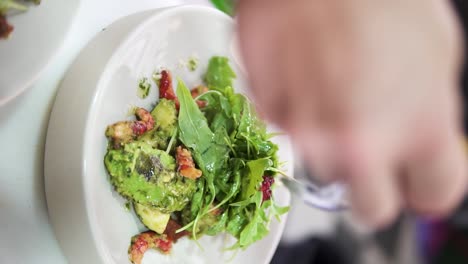 Vertical-handheld-slow-motion-shot-of-a-delicious-salad-with-seafood,-avocado-and-lettuce-leaves-finished-with-olive-oil-in-an-upscale-restaurant