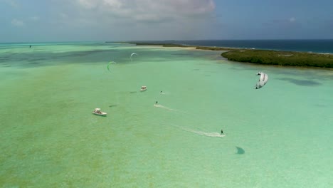 Aerial-turn-around-kitesurfers-slide-on-flats-sea-waters-,-mangrove-and-boats-in-salinas,-Los-Roques