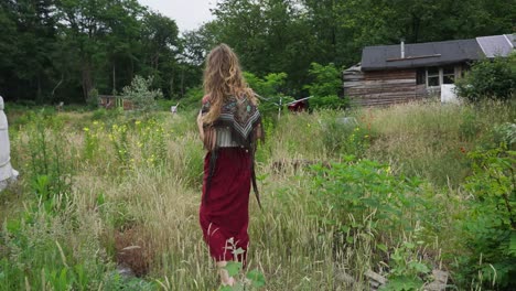 Beautiful-Off-grid-woman-Female-Eco-Conscious-Hippie-Walking-Through-Wild-Gardens-Next-To-Yurt-in-ecovillage