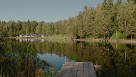 POV-Walking-To-Wooden-Bridge-at-Kypesjön-Lake-With-Open-Air-Yard-in-Background,-Borås,-Sweden---Wide-Shot-Tracking-Forward-and-Truning-Left