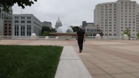 Caucasian-man-walking-in-hat-and-black-clothes-on-Monona-Terrace-in-Madison,-Wisconsin