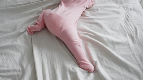 Newborn-baby-girl-first-steps,-crawling-on-bed-sheet-wearing-pink-pajamas