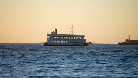 A-vintage-or-20th-Century-steamboat-anchored-in-the-harbor-during-a-golden-sunset---isolated-slow-motion