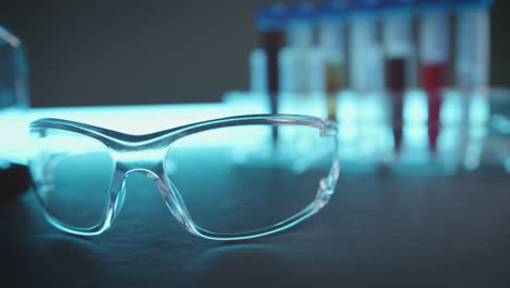 Laboratory-workstation-with-glass-safety-goggles,-measuring-vessels-and-sample-tubes-on-a-bluish-table