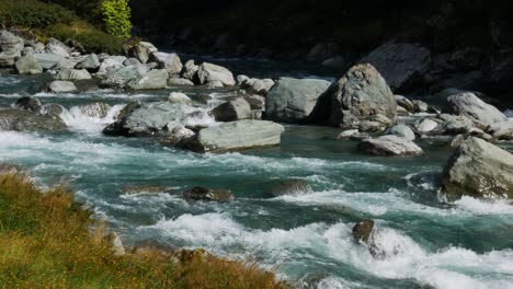 Panning-shot-of-natural-flowing-river-between-rocks-at-sunlight-during-Hike-on-Rob-Roy-Track-in-New-Zealand