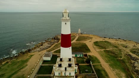 Iconic-lighthouse-building-on-ocean-coastline,-aerial-fly-away-shot