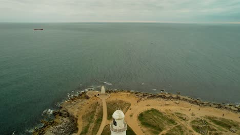 Ship-sailing-in-open-ocean-with-close-up-view-of-red-and-white-lighthouse,-aerial-descend-view