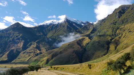 Espectacular-Panorama-Montañoso-Con-Plantas-En-Crecimiento-Y-Río-Natural-Durante-La-Luz-Del-Sol-Y-El-Cielo-Azul-En-La-Cima-De-La-Montaña-Nevada-De-Nueva-Zelanda-En-El-Fondo