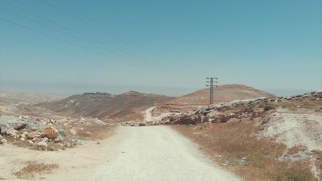 Drone-Volando-Sobre-Un-Camino-En-Una-Colina-En-El-Desierto-Con-Montañas-Alrededor,-Pequeños-Pueblos-En-Los-Montes,-Desierto-De-Judea,-Israel