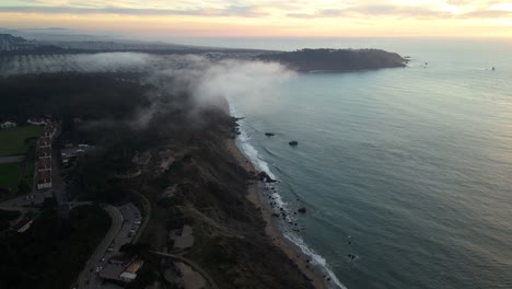 Aerial-drone-view-of-a-foggy,-colorful-sunrise-on-the-coast-of-San-Francisco,-USA