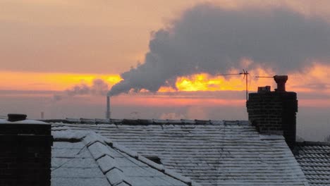 Smoking-industry-chimney-above-icy-winter-home-rooftops-glowing-sunrise-orange-sky