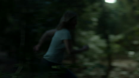 Wide-shot-of-scared-woman-running-through-a-spooky-forest-at-night