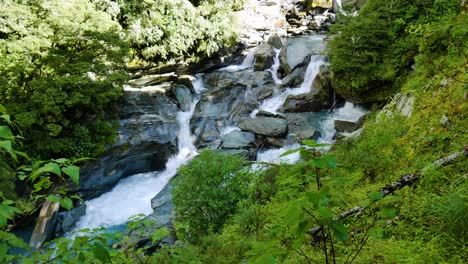 Idyllic-cascade-flowing-waterfall-surrounded-by-mossy-mountains-during-sunny-day---Rob-Roy-Glacier-in-New-Zealand