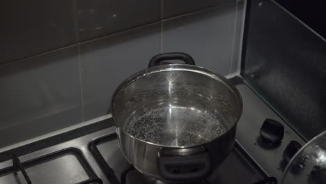 Caucasian-hand-lifts-lid-on-cook-pot-of-hot-water-on-gas-stove-burner