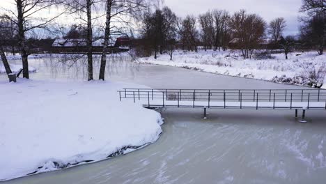 Kleiner-Stadtpark-Mit-Brücke-über-Gefrorenes-Seewasser-In-Der-Wintersaison,-Luftbild