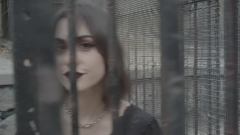 Young-adult-woman-with-dark-makeup-defying-camera-trapped-into-a-cage-gray-tones