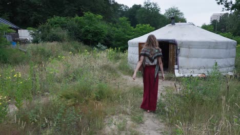 Young-hippie-girl-entering-a-rural-tent-at-an-eco-camping-village,-sustainable-organic-agriculture-and-off-grid-ecovillage