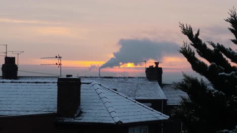 Smoking-industry-chimney-above-frozen-winter-home-rooftops-glowing-sunrise-orange-sky