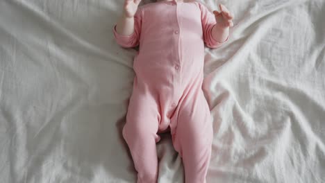 Top-down-closeup-of-playful-unrecognizable-newborn-baby-in-bed,-wear-pink