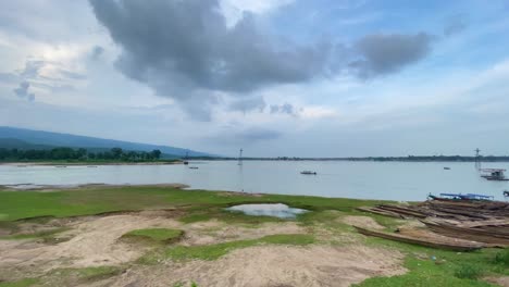 Rural-lake-landscape-with-wooden-boats-and-mountains-in-Bangladesh,-panoramic-pan-view