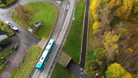 Aerial-top-down-shot-of-driving-Articulated-Bus-driving-on-rural-road-between-colorful-trees-in-Gothenburg,Sweden