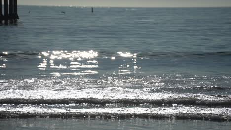 Sunshine-glistening-off-the-ocean-waves-by-a-beach-pier-with-seabirds-over-the-horizon-in-dreamy-slow-motion