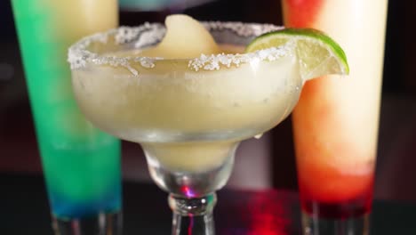 Frosty-frozen-margarita-dressed-with-salt-rim-and-lime-wedge-upstages-two-swirl-margaritas-behind,-close-up-4K