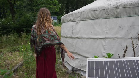 Eco-Conscious-Female-Walking-Away-From-Solar-Panel-next-to-ecovillage-tent-yurt-in-forest,-sustainable-energy,-feminine-power-nature-connection