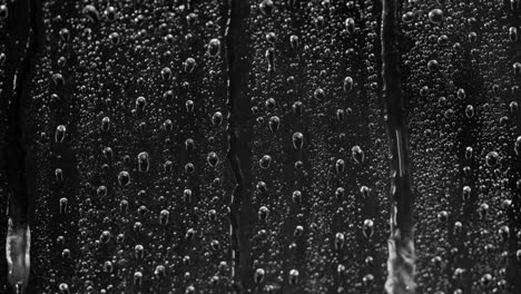 Close-up-rain-on-window,-Water-Drops-following-down-on-black-background