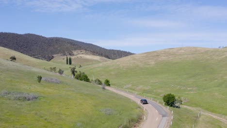 Beautiful-tracking-shot-taken-from-above,-car-driving-through-the-Australian-wilderness-with-some-trees-and-meadows,-no-people,-daylight,-sunny-day