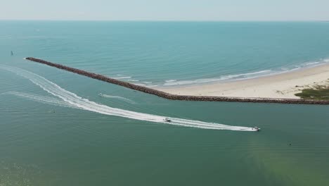 Aerial-tracking-shot-of-speedboats-cruising-into-river-mouth-coming-from-blue-ocean