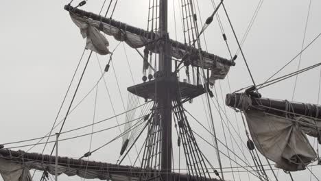 Galleon-Andalucia-replica-ship-detail-tilt-shot-of-the-mainmast,-roundhouse-and-sails-against-the-sun-while-docked-in-Valencia-in-slow-motion-60fps