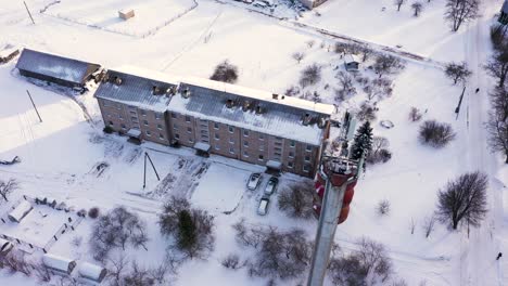 Small-apartment-building-and-tall-tele-communication-tower-in-winter-season,-aerial-ascend-shot