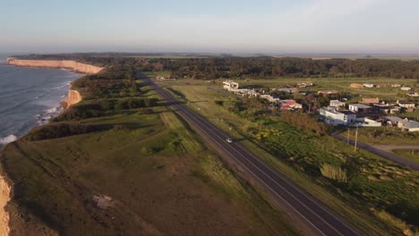 Car-driving-on-coastal-road-beside-ocean,cliffs-and-green-forest-during-sunset-in-Mar-del-Plata,Argentina---Aerial-view