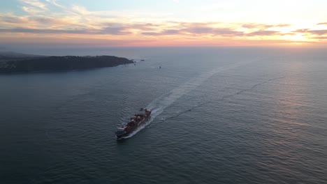 Aerial-view-around-a-bulk-carrier-on-the-coast-of-San-Francisco,-during-sunset---circling,-drone-shot