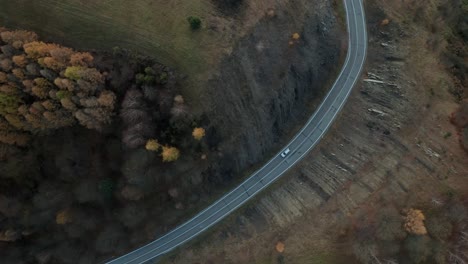 An-aerial-tilt-down-drone-view-of-a-car-driving-on-a-winding-road-running-through-a-canyon-in-late-autumn