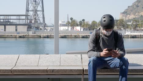 Lonely-young-man-with-protective-mask-and-helmet-chatting-with-mobile-phone