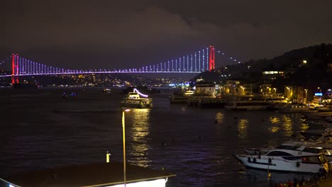 Bunte-Bosporus-Brücke-Bei-Nacht-Mit-Beleuchteten-Booten-Auf-Dem-Meer