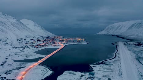 Aerial-backwards-shot-of-lighting-bridge-and-magical-Siglufjordur-City-in-North-Iceland-during-mystic-clouds-at-sky---Beautiful-snowy-evening-in-winter