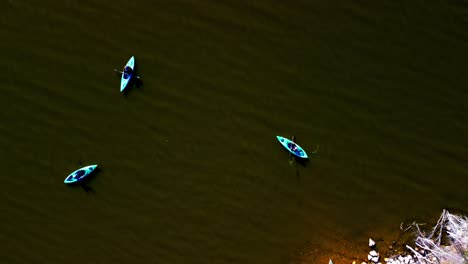 Birds-view-kayakers-forming-a-triangle-approaching-each-other-to-start-paddling-on-lake-from-the-beach-front-rocky-area