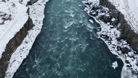 Cold-and-icy-Skjalfandafljot-river-flowing-between-snowy-banks-and-rocks-in-winter---North-Iceland,Europe---Aerial-Tilt-up-shot