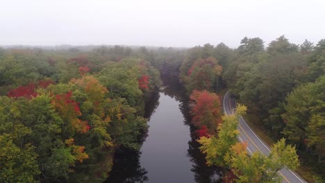Aerial-Foggy-river-with-autumn-foliage-flying-forward-with-road-beside