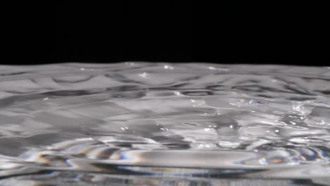 Water-droplets-fall-into-rippling-clear-liquid,-Slowmo-Extreme-Closeup