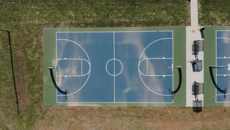 Eine-Statische-Luftaufnahme-Von-Oben-Nach-Unten-Eines-Blauen-Basketballplatzes-Im-Freien-Während-Des-Mittags-Mit-Langen-Schatten-4k